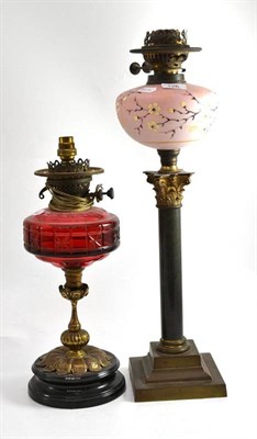 Lot 126 - A brass oil lamp with cranberry glass well, another with opaque pink glass well painted with...