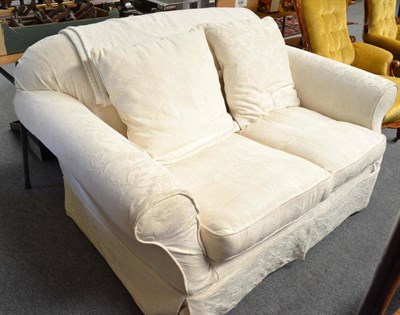 Lot 554 - An upholstered two seater settee with cream loose covers