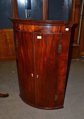 Lot 784 - A George III mahogany bow front hanging corner cupboard with H brass hinges, enclosing shelves