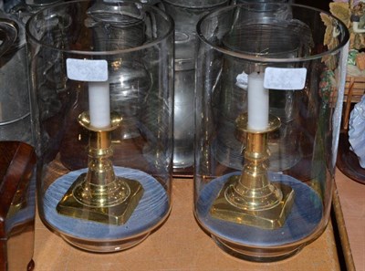 Lot 323 - A pair of clear glass bell jars containing a brass candlestick