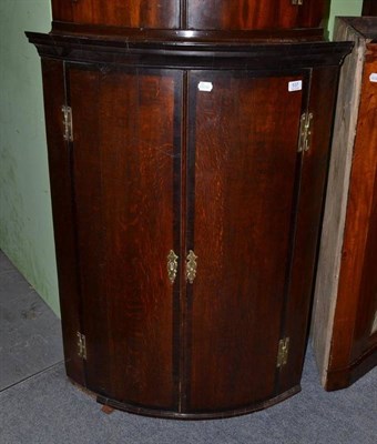 Lot 537 - A George III bow fronted oak wall hanging corner cupboard, cross-banded in mahogany