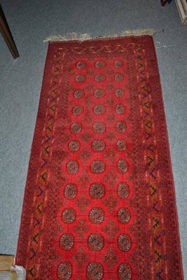 Lot 598 - Afghan Mori narrow runner, the madder field with three rows of octagonal guls enclosed by...