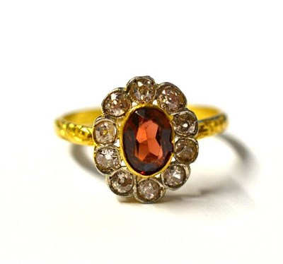 Lot 270 - A Garnet and Diamond Cluster Ring, the oval cut garnet in a yellow collet setting, within a...