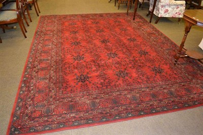 Lot 428 - Large machine made carpet of Afghan design, the tomato red field with columns of stylised...