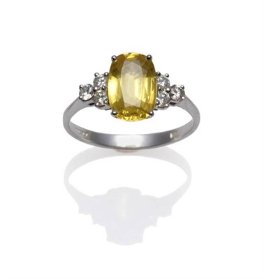 Lot 286 - An 18 Carat White Gold Yellow Sapphire and Diamond Ring, the oval mixed cut yellow sapphire flanked