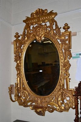 Lot 470 - An ornate giltwood and gesso wall mirror with candle sconces and bevelled oval plate