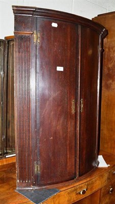 Lot 561 - A Georgian stained oak and mahogany bow fronted corner cupboard