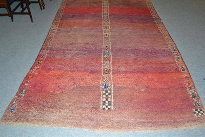 Lot 661 - Berber Moroccan carpet, the abrashed pale aubergine field with a single band of geometric...