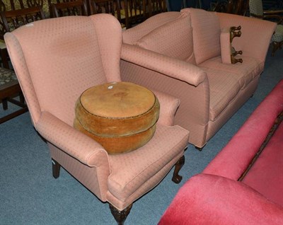 Lot 510 - A salmon upholstered drop end settee, a matching wing back chair and a leather poof