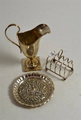 Lot 181 - A silver cream jug with scroll handle, a small toast rack, a silver foliate decorated circular dish