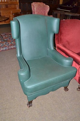 Lot 580 - An early 20th century wing back chair, upholstered in green leather with flared sides, raised...