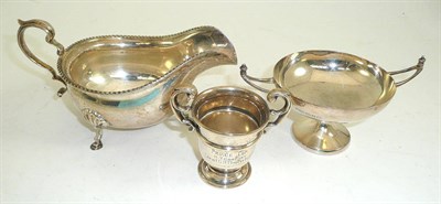 Lot 309 - A silver sauce boat on hoof feet, silver twin handles bon bon dish and miniature trophy