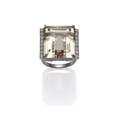 Lot 362 - An 18 Carat White Gold Peach Coloured Topaz and Diamond Ring, the emerald-cut topaz with a row...