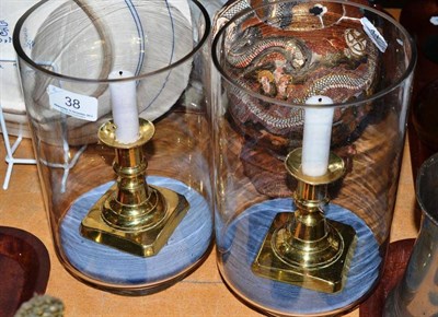 Lot 38 - A pair of clear glass bell jars containing a brass candlestick