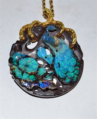 Lot 264 - A black opal with matrix pendant, carved as a peacock and bloom, on a textured branch effect frame