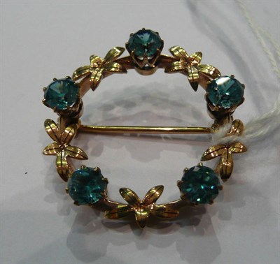 Lot 174 - A gold wreath shaped brooch with blue zircons