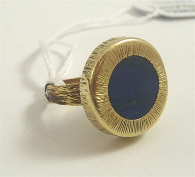 Lot 324 - # A lapis lazuli ring, the central lapis lazuli disk in a textured border to similar shoulders...