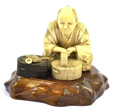 Lot 134 - A Japanese Ivory and Wood Okimono, Meiji period, as a millstone cutter, the seated figure holding a