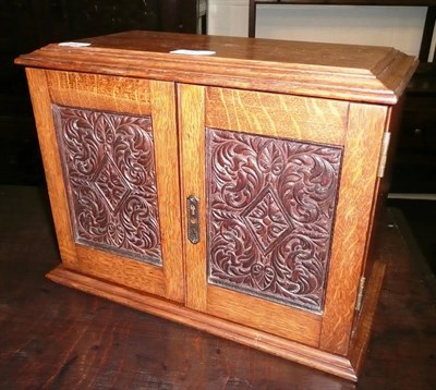 Lot 383 - An Edwardian oak smoker's cabinet with carved doors