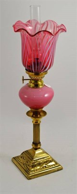 Lot 127 - A brass oil lamp with Corinthian column and cranberry glass shade