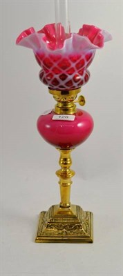 Lot 128 - A brass oil lamp with Corinthian column and cranberry glass shade