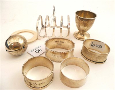 Lot 80 - Silver toast rack, four silver napkins rings, silver egg cup and a silver bell rattle