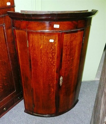 Lot 602 - A George III oak and mahogany crossbanded bowfront hanging corner cupboard