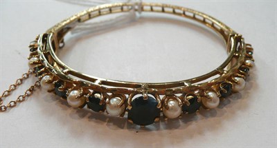 Lot 327 - A 9 Carat Gold Sapphire and Cultured Pearl Bangle, a central oval mixed cut sapphire to a row...