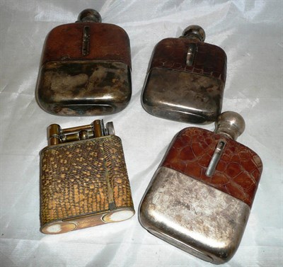 Lot 486 - A jumbo petrol lighter with snakeskin sleeve, together with three hipflasks, one with silver mounts