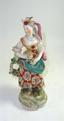 Lot 211 - A Derby figure of a girl depicted wearing an elaborate headdress, floral dress on scroll...