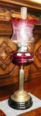 Lot 426 - A brass oil lamp with ruby glass reservoir and cranberry-tinted shade