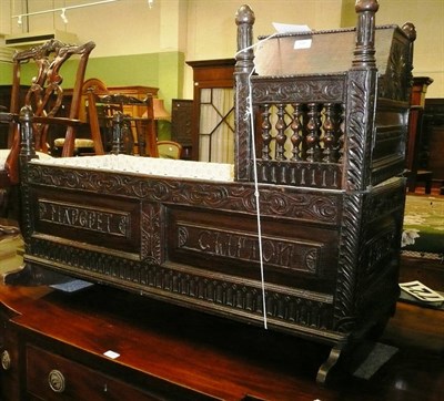 Lot 597 - A carved oak cradle with balustraded canopy the side panels carved Margaret Clifton and Thomas...