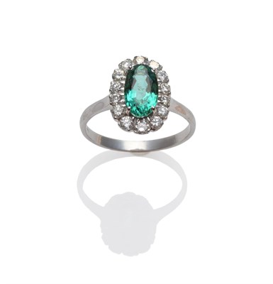 Lot 225 - An 18 Carat White Gold Emerald and Diamond Ring, the oval mixed cut emerald within a border of...