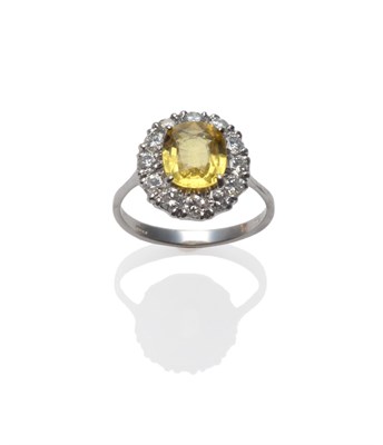 Lot 235 - An 18 Carat White Gold Yellow Sapphire and Diamond Cluster Ring, the oval mixed cut sapphire within