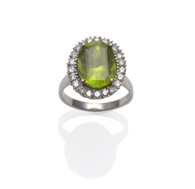 Lot 257 - An 18 Carat White Gold Peridot and Diamond Cluster Ring, an oval cut peridot within a border of...