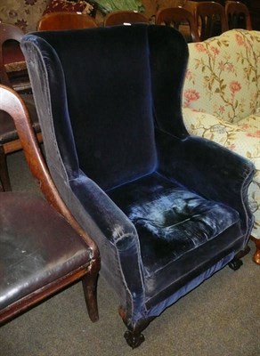 Lot 676 - A blue velvet wing armchair on claw and ball feet