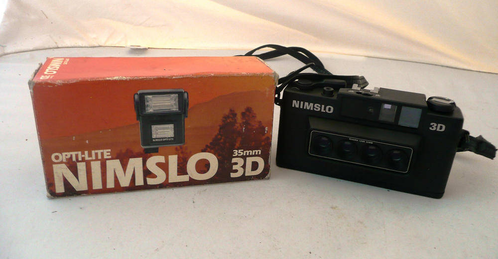 Lot 1233 - A Nimslo 3D Camera, with black plastic body, Quadra 30mm lens, leather case and boxed Opti-lite...