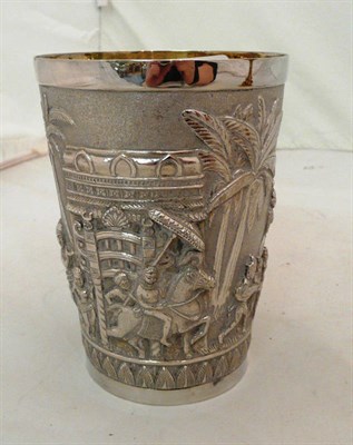 Lot 394 - An Indian silver coloured metal beaker richly chased and cast with figures worshipping a deity,...