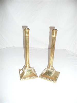 Lot 123 - A pair of George III brass candlesticks with reeded columns on square bases, circa late 18th...