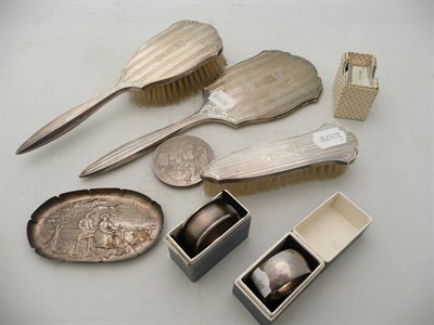 Lot 190 - Three silver napkin rings, a silver-backed three piece dressing table set, a silver pin dish...