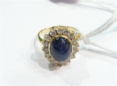 Lot 337 - A synthetic star sapphire and diamond cluster ring, the cabochon sapphire within a border of...