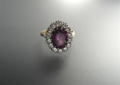 Lot 306 - A Ruby and Diamond Cluster Ring, the oval mixed cut ruby sits above a gallery of round...