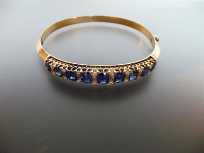 Lot 311 - A Sapphire and Diamond Bangle, graduated oval mixed cut sapphires are spaced by pairs of...