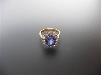 Lot 338 - An 18 Carat Gold Sapphire and Diamond Cluster Ring, an oval mixed cut sapphire within a border...