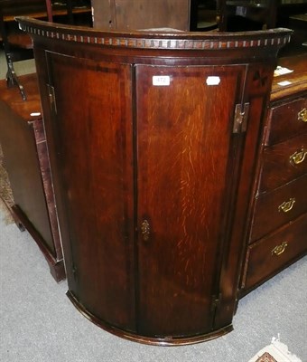 Lot 472 - A George III oak mahogany banded bow front corner cupboard, with dentil cornice, two doors...