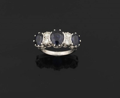 Lot 387 - A Sapphire and Diamond Ring, three graduated oval mixed cut sapphires are spaced by pairs of...