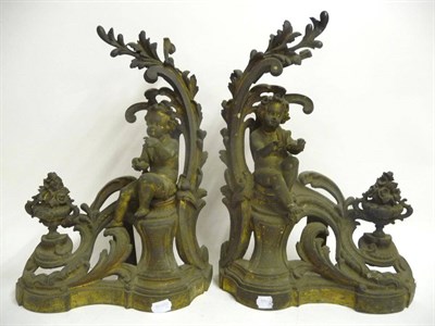 Lot 1295 - A Pair of Gilt Brass Fire Dogs, French, circa 1850, each cast as infants seated amongst pierced and