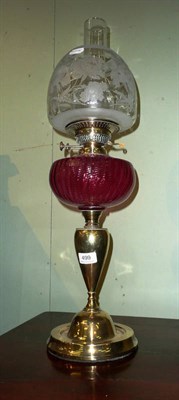 Lot 499 - Cranberry oil lamp and shade on brass base