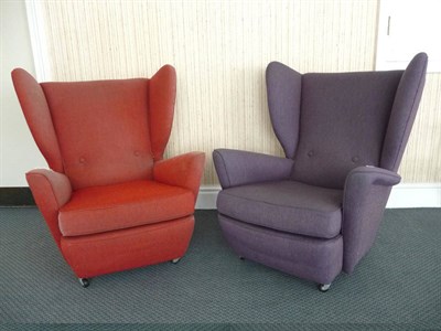 Lot 1730 - A Pair of 1960s Wing Armchairs, of shaped design, one upholstered in purple, the other in red...