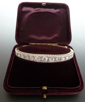 Lot 234 - A Graduated Diamond Line Bangle, the old cut diamonds held in claw settings within a white...